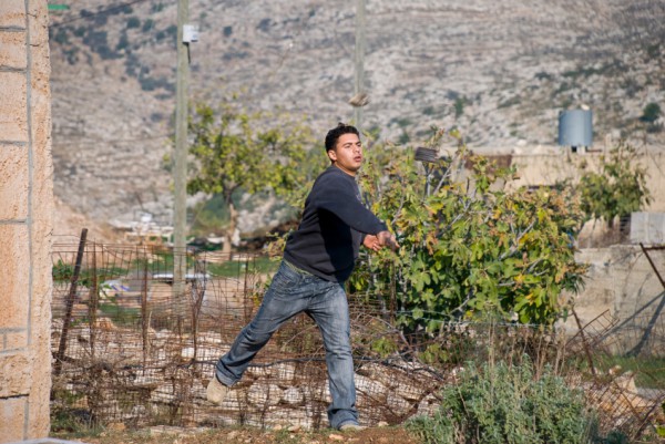A Palestinian hurls a rock at soldiers protecting the settlement Palestinian-Youth-Rock