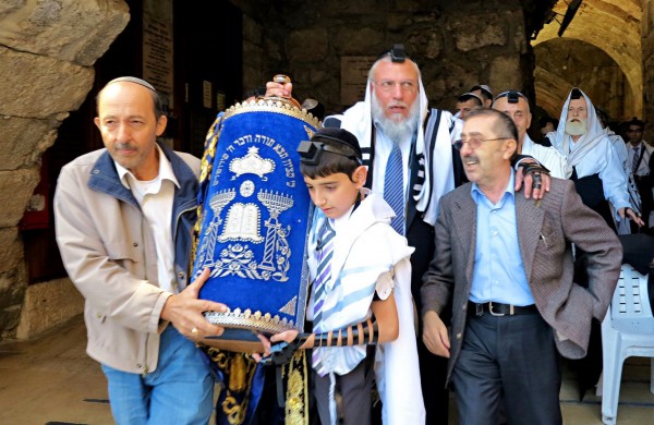 A Jewish father and son at the Western (Wailing) Wall in Jerusalem share the burden of carrying the heavy Torah scroll. A Jewish father and son at the Western (Wailing) Wall in Jerusalem share the burden of carrying the heavy Torah scroll.